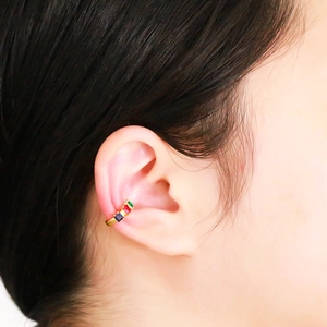 Detailed close-up of a gold U-shaped ear cuff set with green, red, and blue gemstones