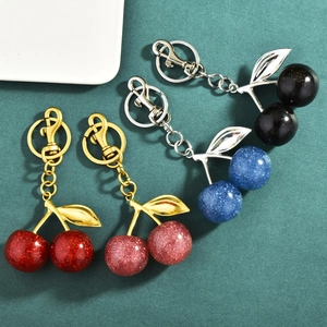 Sparkly resin cherry keychains in four colors with gold leaves on dark green background