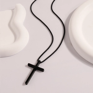 Macro detail of a minimalist matte black stainless steel cross pendant and beaded chain
