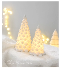 Macro shot of white ceramic Christmas tree lamps with warm lights on snowy base