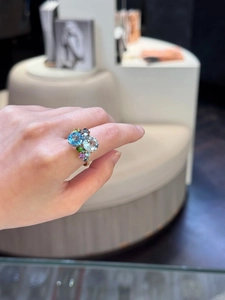 Close-up of golden geometric hollow ring set with blue and purple zircon stones on finger