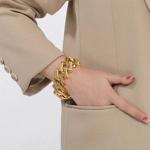 Gros plan d'un bracelet gourmette doré porté par un mannequin en veste beige