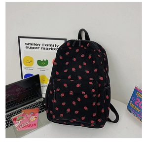 Close-up of black corduroy backpack with red strawberry print and ribbed texture details