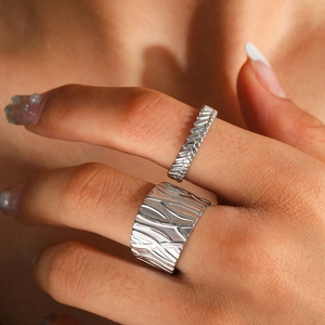 Close-up of two irregular textured silver stainless steel rings on fingers