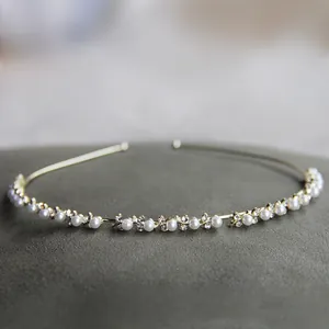 Dettaglio macro del cerchietto dorato con perle e strass su superficie grigia