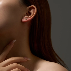 Close-up of heart-shaped gold stud earring with purple gemstone on a model ear