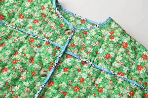 Detail of floral quilted jacket featuring green fabric with blue textured trim and wooden buttons