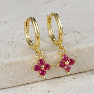 Detail of S925 silver gold clover earring with red zircon stones on stone surface
