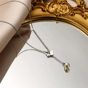 Détail du collier en acier titane argenté avec pendentif papillon et perle sur miroir