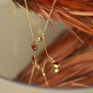 Macro shot of gold-plated heart necklace with red tassel and artistic mirror reflection