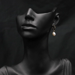 Elegant gold hoop earrings with white baroque pearl drop on minimalist black display
