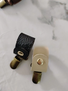 Details der Hutclips aus schwarzem und beige Leder mit goldenen Schnallen auf Marmorboden