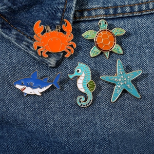Group of 5 colorful sea animal enamel pins on denim fabric including crab and turtle