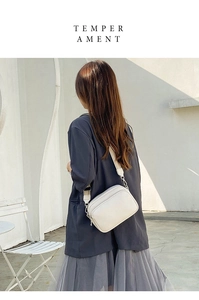 Street style view of a white leather shoulder bag worn by a model against a white wall