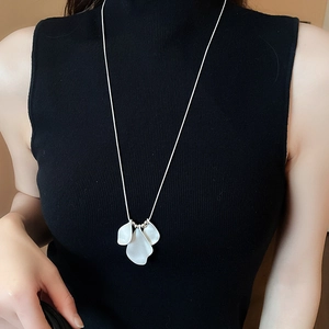 Detail of white petal pendant necklace worn on black sweater for elegant style