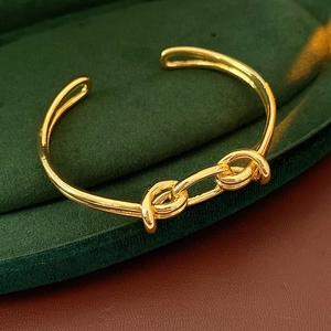 Detail view of gold-plated knot bangle on green velvet jewelry box with glossy mirror finish