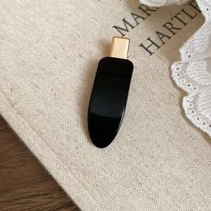 Close-up of elegant black oval hair clip with gold metal grip on rustic background