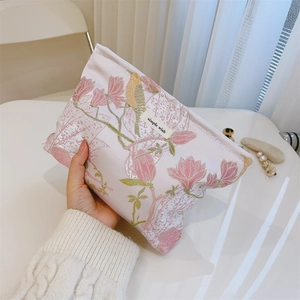 Detail der rosa Kosmetiktasche mit Blumen-Vogel-Stickerei und weißem Markenetikett