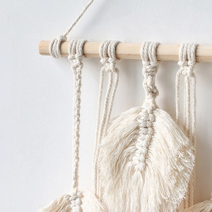 Close-up of handmade macrame feather leaf tapestry with natural wood rod detail