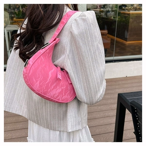 Bright pink crescent shoulder bag in wrinkled patent leather worn by a model on a terrace