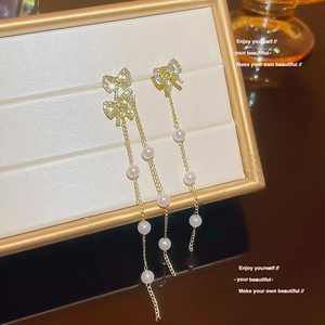 Close-up of elegant gold long tassel earrings with pearls and bowknot on jewelry box