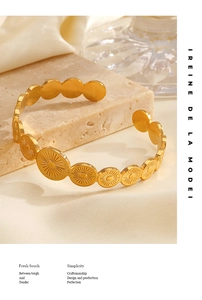 Detailed close-up of a gold cuff bracelet with engraved sunflower patterns on stone