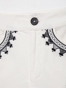 Macro detail of white vest with black button and elegant lace embroidery on the pocket
