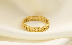 Close-up of golden stainless steel cuban link ring on soft off-white satin fabric