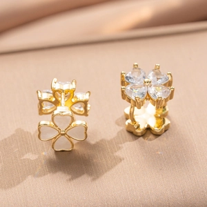 Elegant gold clover earrings with clear heart-shaped zirconia on a warm silk background