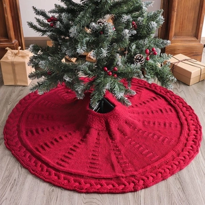 Detail of red knitted Christmas tree skirt featuring braided patterns on wood floor