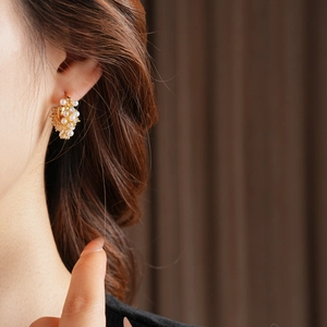 Close-up of elegant gold U-shaped earrings with pearls and zircons on a model's ear