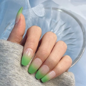 Close-up of glossy gradient press-on nails from nude to green in a long coffin shape