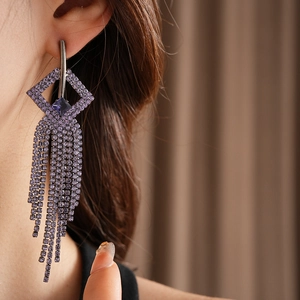 Detail of silver drop earrings with geometric diamond cutouts and long purple tassels