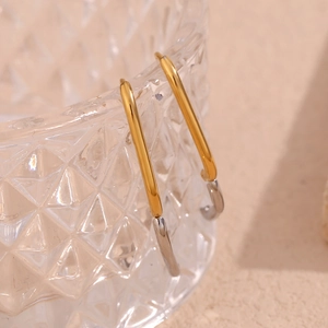 Detailed close-up of two-tone oval hoop earrings in gold and silver on a glass rim