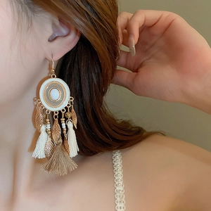 Detail shot of bohemian tassel earrings with white beads and golden leaf charms