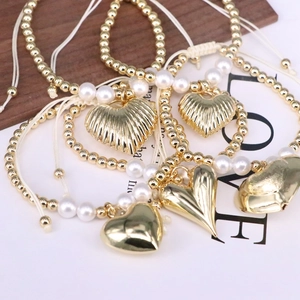 Beaded gold heart pendant bracelet set with white pearls on a rustic wood background