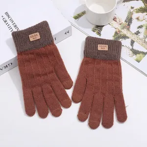 Close-up of caramel knit gloves with gray ribbed cuffs and a leather logo brand patch