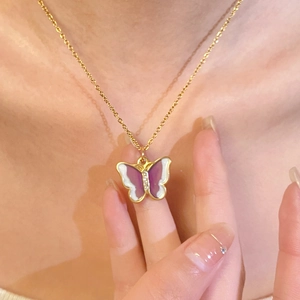 Close-up of golden butterfly pendant with purple and white enamel on a delicate chain