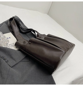 Detail of dark brown leather tote bag on grey suit and white textured fabric backdrop
