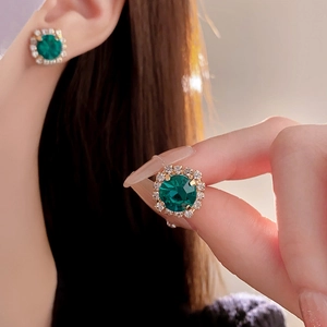 Close-up of green gemstone earrings with gold base and white diamond halo on model