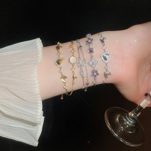 Close-up of elegant zircon heart and floral charm bracelets worn with a stylish cocktail glass