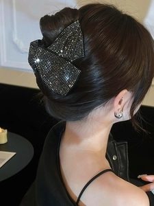 Detail of elegant black fabric bow hair claw with sparkling rhinestones on model