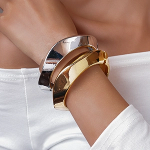 Close-up of wide polished gold and silver metal bangles on a model's wrist