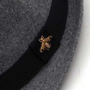 Close-up of wool fedora hat with black ribbon and golden bee metal emblem detail