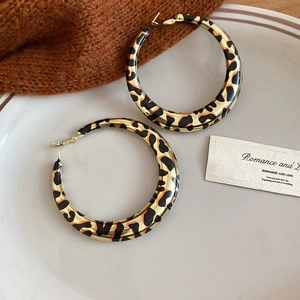 Macro detail of retro leopard print hoop earrings with gold metal edges on a ceramic plate
