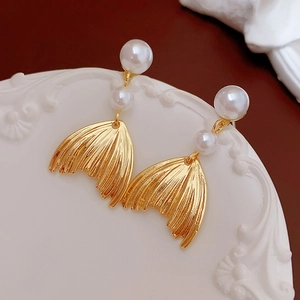 Detail of gold fish tail earrings with white pearls on a white textured stand