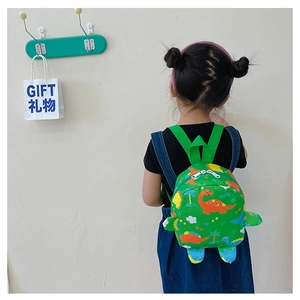 Green kids dinosaur backpack worn by a toddler girl against a clean white wall