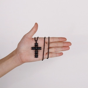 Detail of hand holding a black stainless steel layered cross pendant with twist chain