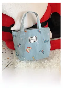 Détail du sac en toile bleue avec broderie papillon et poignées en sangle confortables