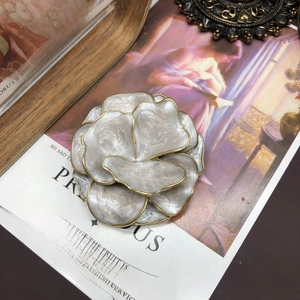 Detailed close-up of white enamel flower brooch with gold edges on vintage book pages